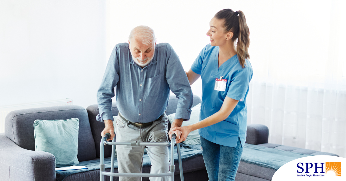 A professional caregiver helps an older man walk with a walker, showing how having a caregiver help a loved one stay mobile safely can help avoid hospital readmissions.