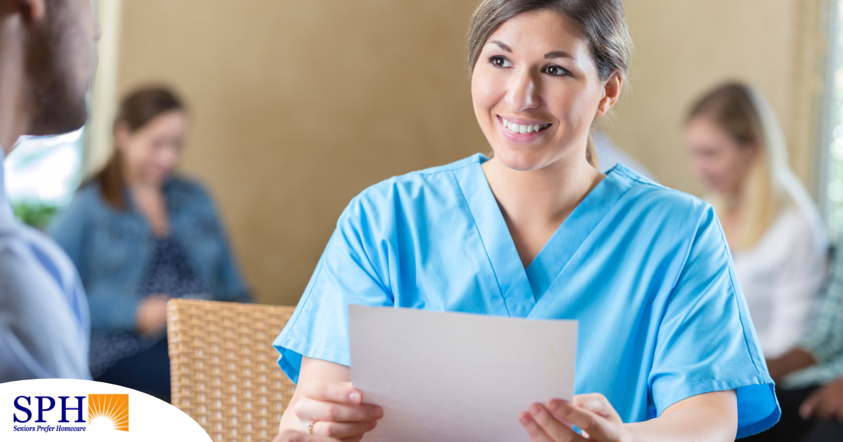 A woman in scrubs holds a paper while interviewing with someone else, representing how a solid caregiver resume can get you to an interview.