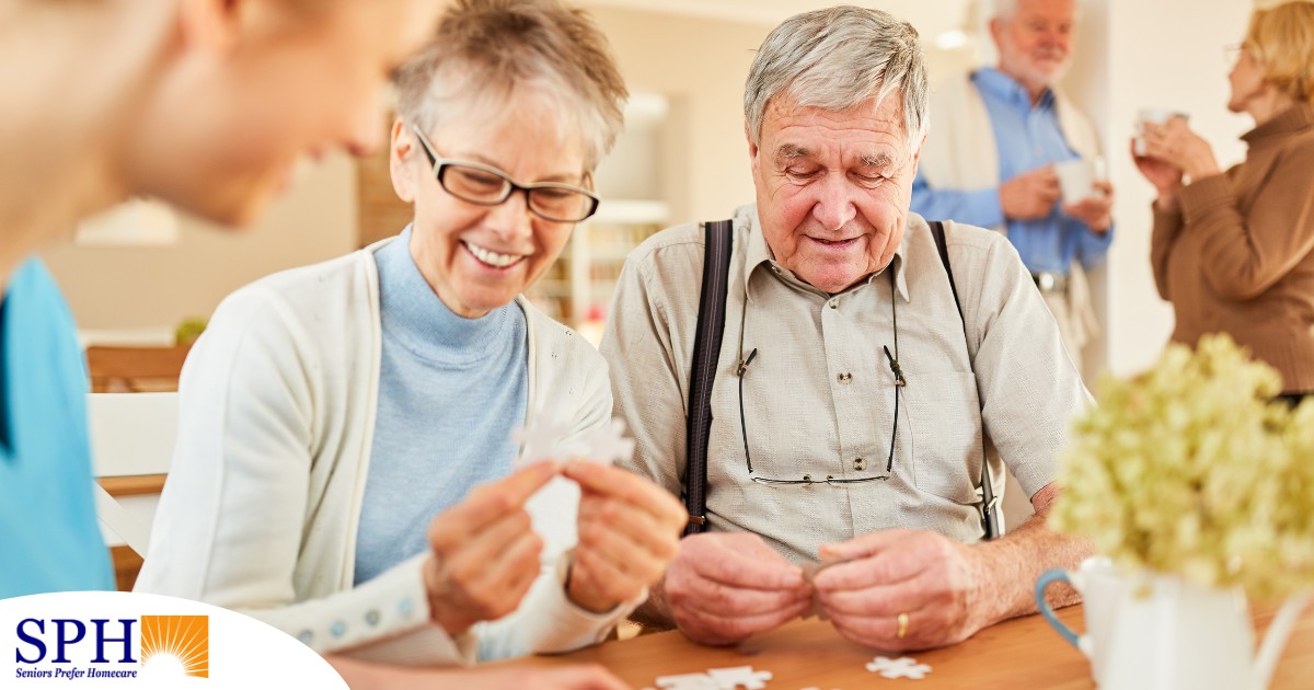 An older couple works on a puzzle with a caregiver, representing the kind of activity that helps those with dementia and also representing Alzheimer’s and Brain Awareness Month.