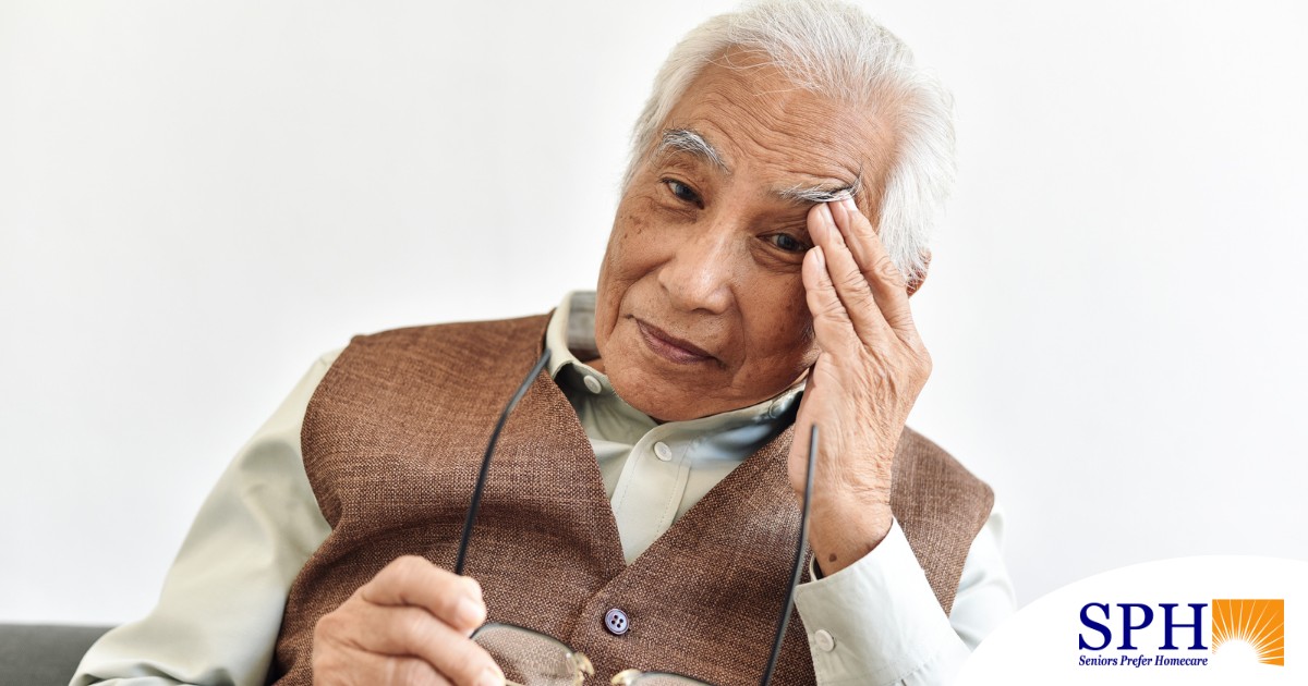 An older adult holds his head and his glasses representing vision problems like macular degeneration.