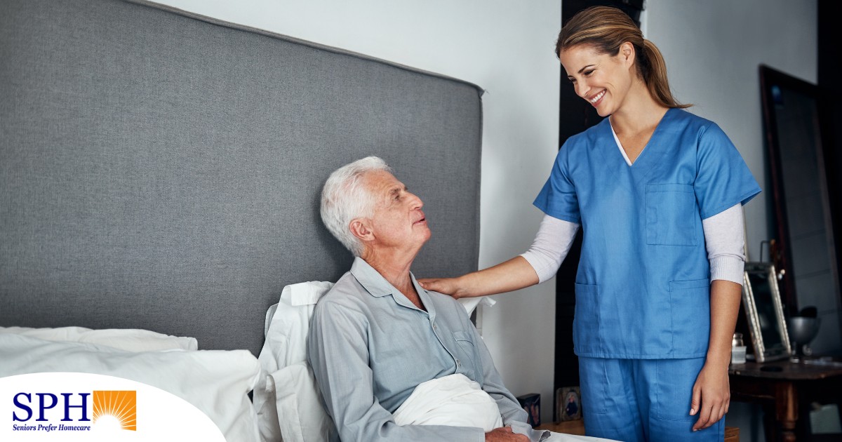 A caregiver smiles at an older client in bed, representing the compassion involved in being a live-in caregiver.