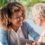 A caregiver smiles at an older client in a chair, representing the joy that can come from a healthy work-life balance.