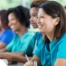 Several students in scrubs happily attend a class, representing caregiver training.