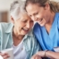 A woman in scrubs laughs with a senior woman, representing how caregiving can be a great career choice.