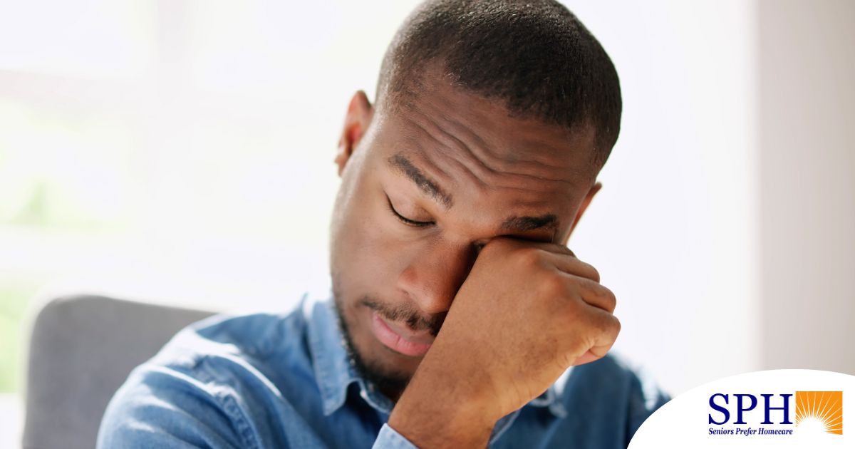 A man tiredly rubs his eyes, representing the exhaustion that can come with family caregiving.