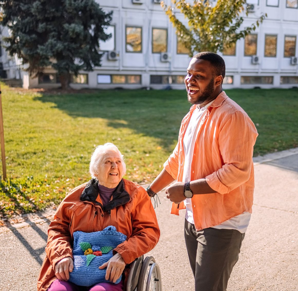Transportation in New Hope (1) Caregiver walking beside a smiling senior woman in a wheelchair outdoors, reflecting compassionate Transportation in New Hope support services.